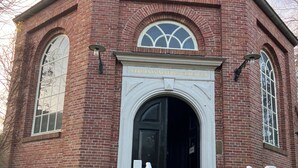 Un bâtiment en briques avec une porte noire, des marches blanches et une enseigne sur laquelle on peut lire : « VIRGINIS MATRIS CLAUSAULA ».