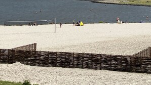 Une plage avec un filet de volley-ball, une tente jaune et un phare en arrière-plan.