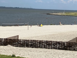 Ein Strand mit einem Volleyballnetz, einem gelben Zelt und einem Leuchtturm im Hintergrund.