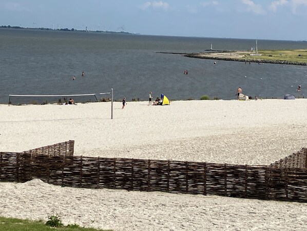 Une plage avec un filet de volley-ball, une tente jaune et un phare en arrière-plan.