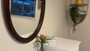 Ein Badezimmer mit einem weißen Waschtisch, einem großen Spiegel, einer kleinen Vase mit einer Pflanze und einem Regal mit einer Ananas und einem Schild.