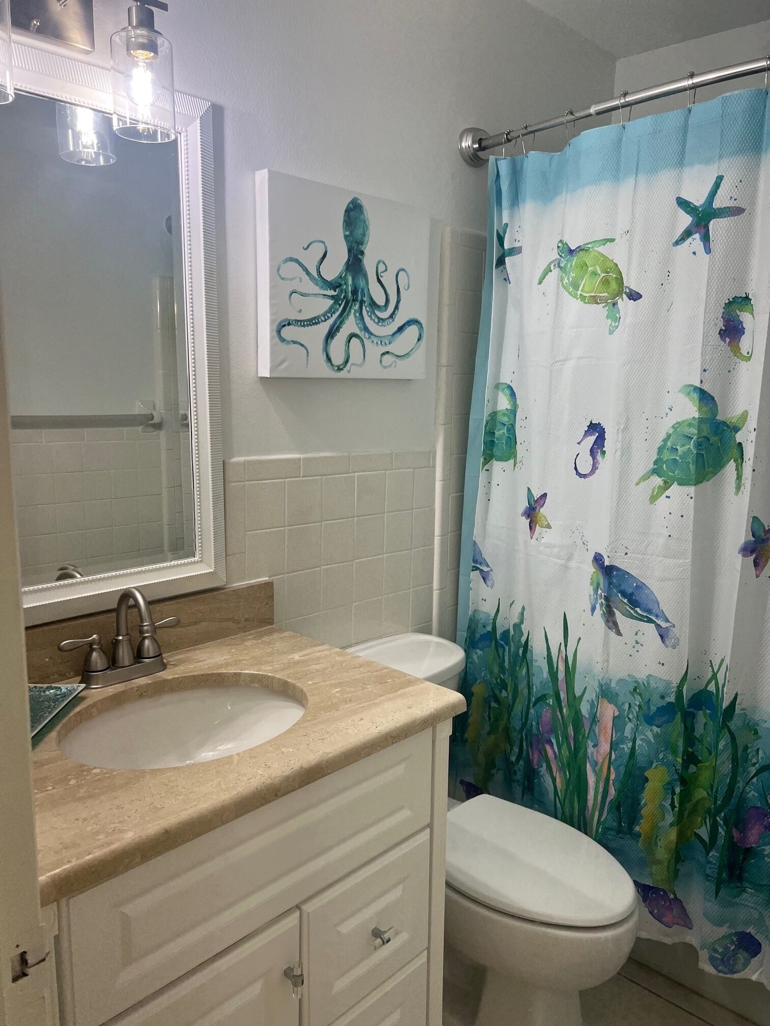 Een badkamer met een wastafelmeubel met dubbele wastafel, een toilet en een douchegordijn met afbeeldingen van zeedieren.