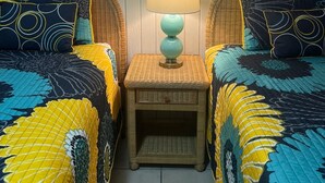 Ein Zimmer mit zwei Betten, jedes mit einer gemusterten Tagesdecke, einem kleinen Nachttisch mit Lampe und einem an der Wand befestigten Spiegel.