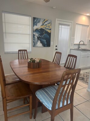 Un coin repas avec une table et des chaises en bois, un tableau accroché au mur et une cuisine en arrière-plan.