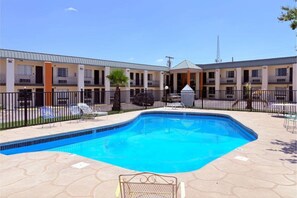 A motel with a swimming pool, outdoor seating, and a fenced patio area.
