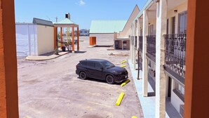 A parking lot with a black SUV, a covered area, and a building with a green roof and balconies.