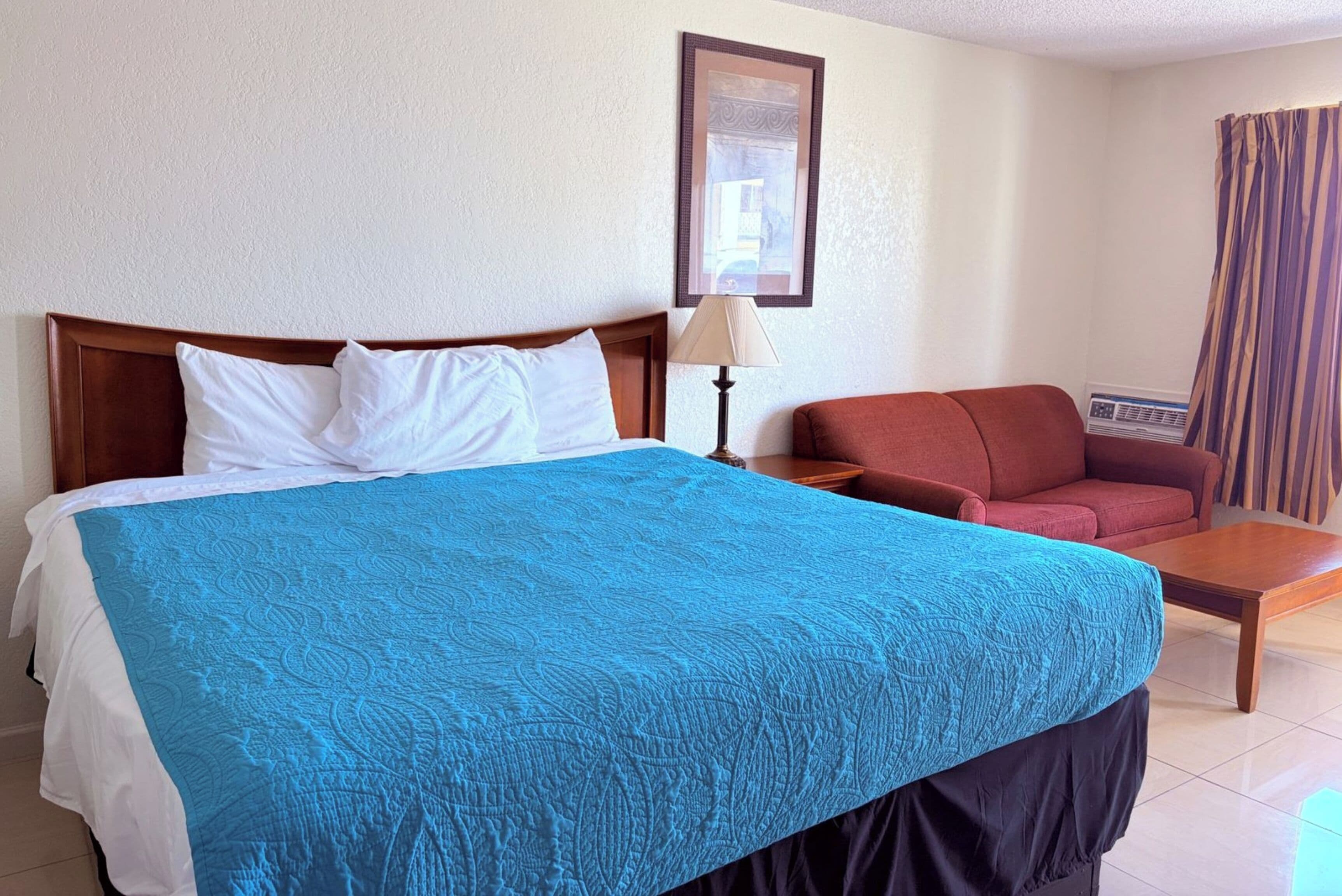A hotel room with a large bed, a red sofa, a small table, and a wall-mounted heater.