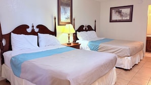A hotel room with two beds, a nightstand with a lamp, and two framed pictures on the wall.