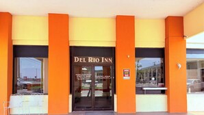 The exterior of Del Rio Inn with a yellow facade, large glass entrance, and a sign indicating a key drop-off point.