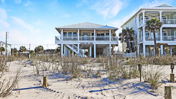 Una proprietà fronte spiaggia con una struttura a due piani e un balcone, con un cartello che recita 'Above the Sand'.