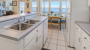 Una cucina con un lavello doppio, mobili bianchi e un'area pranzo con sedie blu.