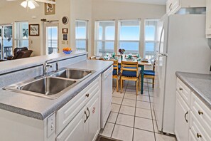 A kitchen with a double sink, white cabinets, and a dining area with blue chairs.