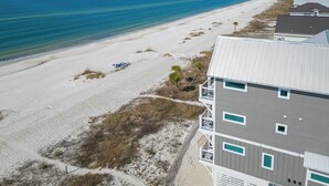 Une propriété située en bord de mer, dotée d’une plage de sable, offrant une vue dégagée sur l’océan, et comprenant un bâtiment moderne avec de nombreuses fenêtres et des balcons.