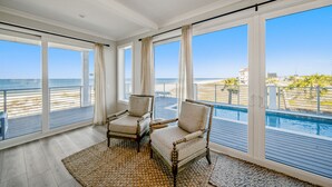A room with large windows, a pool, and two chairs. - Ginger Snap: 5 BR Beachfront Home- Elevated Pool, Pet Friendly, Sleeps 20! (St. Joe Beach)