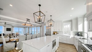 A modern kitchen with white cabinetry, a large island, stainless steel appliances, and pendant lighting. - Ginger Snap: 5 BR Beachfront Home- Elevated Pool, Pet Friendly, Sleeps 20! (St. Joe Beach)