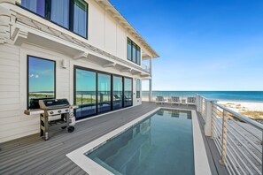 A modern house with a pool, a barbecue, and a view of the beach.