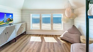 A room with a large window overlooking the beach, a TV on a cabinet, and a cozy seating area.