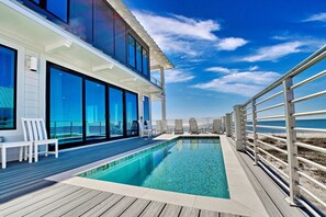 A modern outdoor swimming pool with a wooden deck, large glass windows, and a view of the ocean. - Whit's End:  Luxury Beachfront Home with an Elevated Pool! Pet Friendly! (St. Joe Beach)