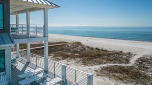 A beach house with a balcony overlooking the ocean, featuring sun loungers and a view of the beach.