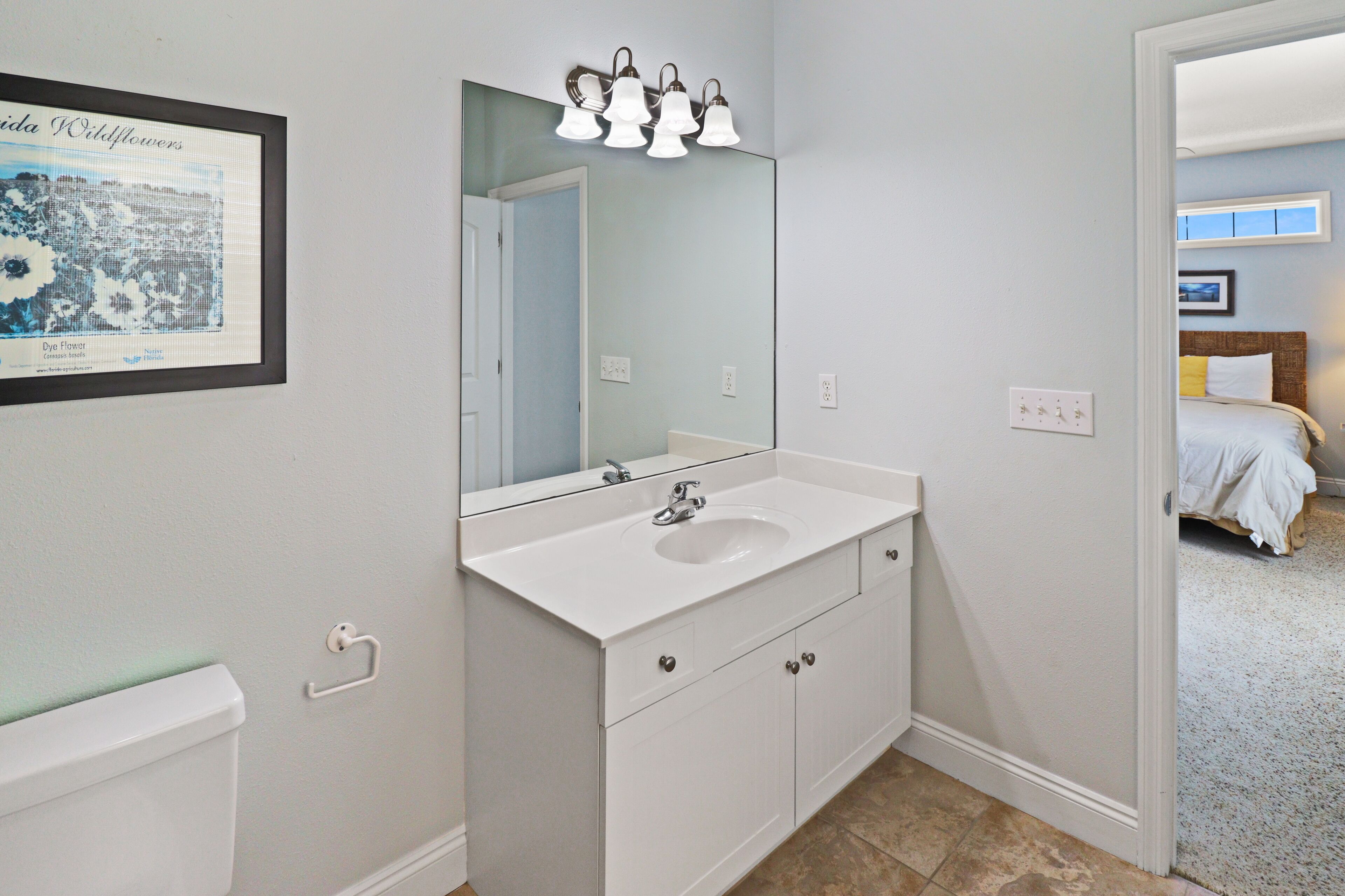 A bathroom with a white sink, a mirror, and a framed picture on the wall.
