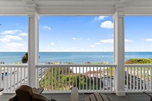 A covered porch with a view of the ocean and beach.