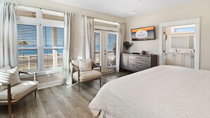 A bedroom with a large bed, a chair, a desk, and a TV. - Living the Dream MB: 4th of July week available as a Friday or Saturday check in (Mexico Beach)