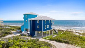 Un edificio azul de dos pisos con balcón, ubicado en una playa con vista al océano.