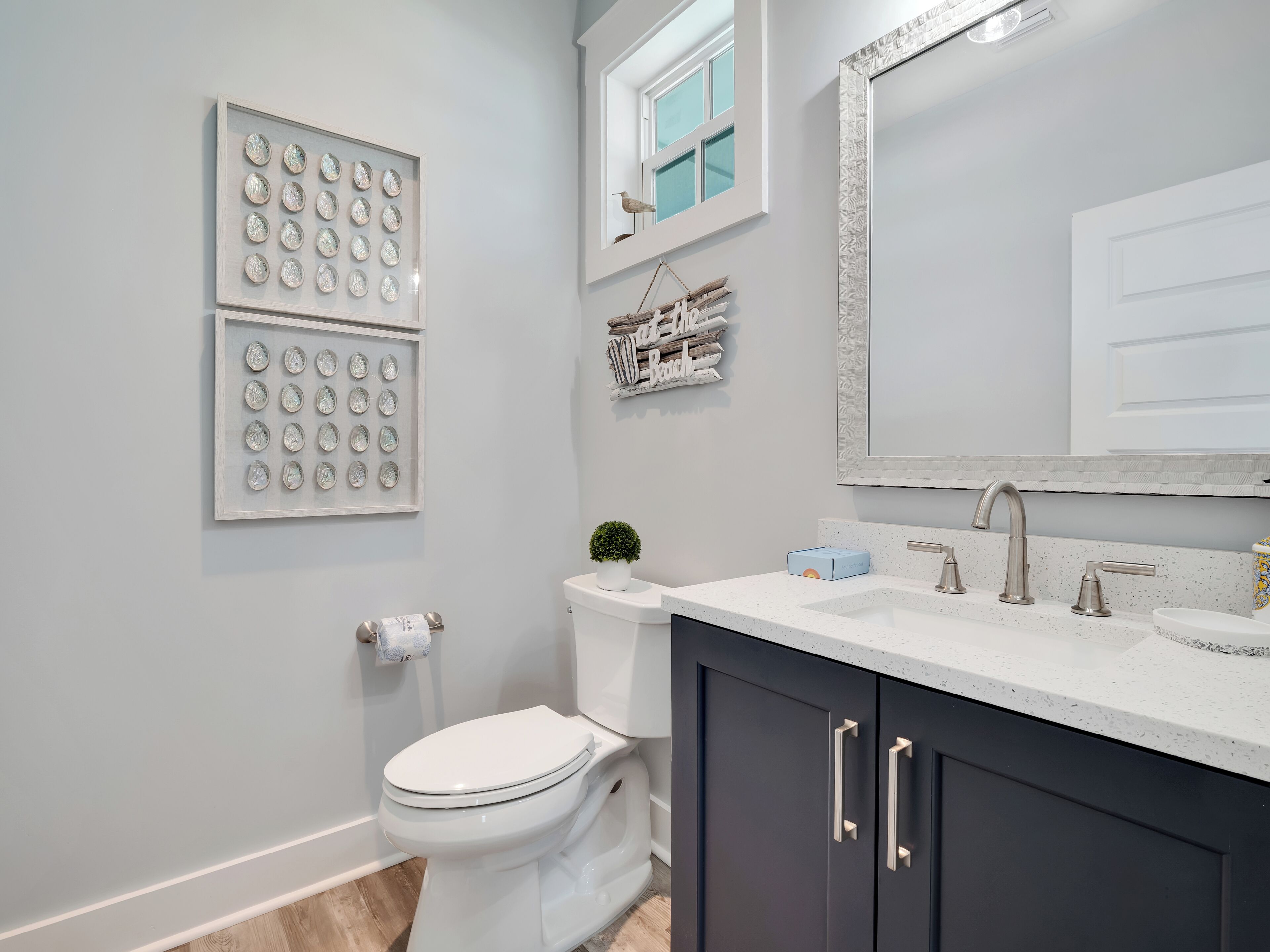 A modern bathroom with a toilet, sink, and mirror. There are framed pictures on the wall and a small plant on the counter.