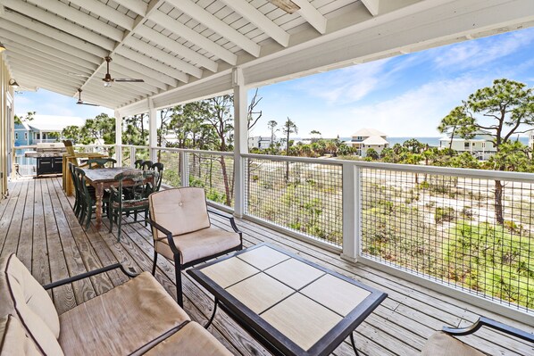 A covered outdoor area with a wooden deck, seating, and a view of the beach and ocean.