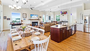 Una cocina amplia con piso de madera, un área de comedor con sillas blancas y una isla grande con un lavamanos.