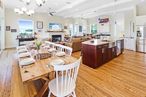 Une cuisine spacieuse avec un plancher en bois, un coin repas avec des chaises blanches et un grand îlot central doté d’un évier.