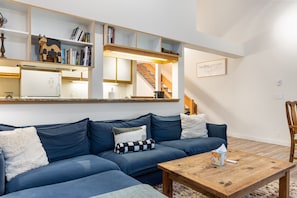 A modern living room with a blue sectional sofa, wooden coffee table, and built-in shelving with books and decorative items. - Outpost: Balsam Lodge B7 (Wilson)