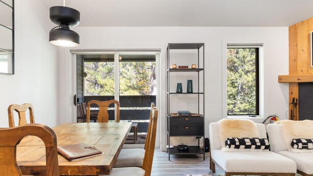 A modern dining area with a wooden table and chairs, a black pendant light, and a bookshelf with decorative items. - Outpost: Balsam Lodge B7 (Wilson)