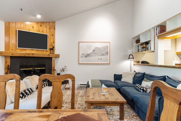 A living room with a fireplace, a sofa, a coffee table, and a TV mounted on the wall.