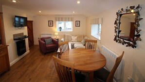 Un salon chaleureux avec une cheminée, un téléviseur fixé au mur, une table à manger avec des chaises et un grand miroir sur le mur.