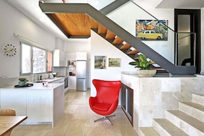 A modern kitchen with a central island, a red chair, and a staircase leading to a dining area.