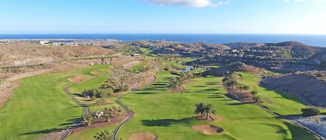 Un campo de golf con vistas despejadas al océano y colinas al fondo.