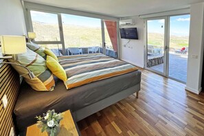 A bedroom with a large bed, a TV, and a view of a patio with outdoor seating.