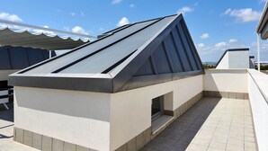 Eine moderne Dachterrasse mit geneigter Dachkonstruktion, einem kleinen Fenster und einem gefliesten Boden.