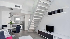 Ein moderner Wohnbereich mit Treppe, Essplatz und Fernseher auf einer weißen Konsole.
