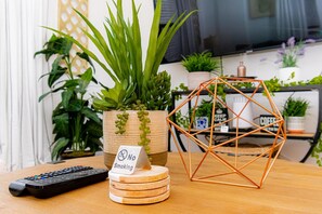 Mesa de madeira com planta em vaso, escultura metálica geométrica, um controle remoto e um aviso de 'No Smoking'.