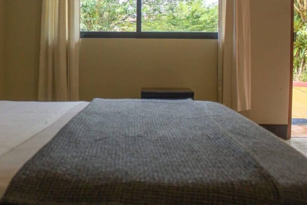 Ein Hotelzimmer mit Bett, einem Fenster mit Vorhängen und Blick ins Grüne.