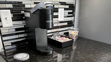 A kitchen with a black countertop, a Keurig coffee maker, a coffee pod holder, and a trash can.