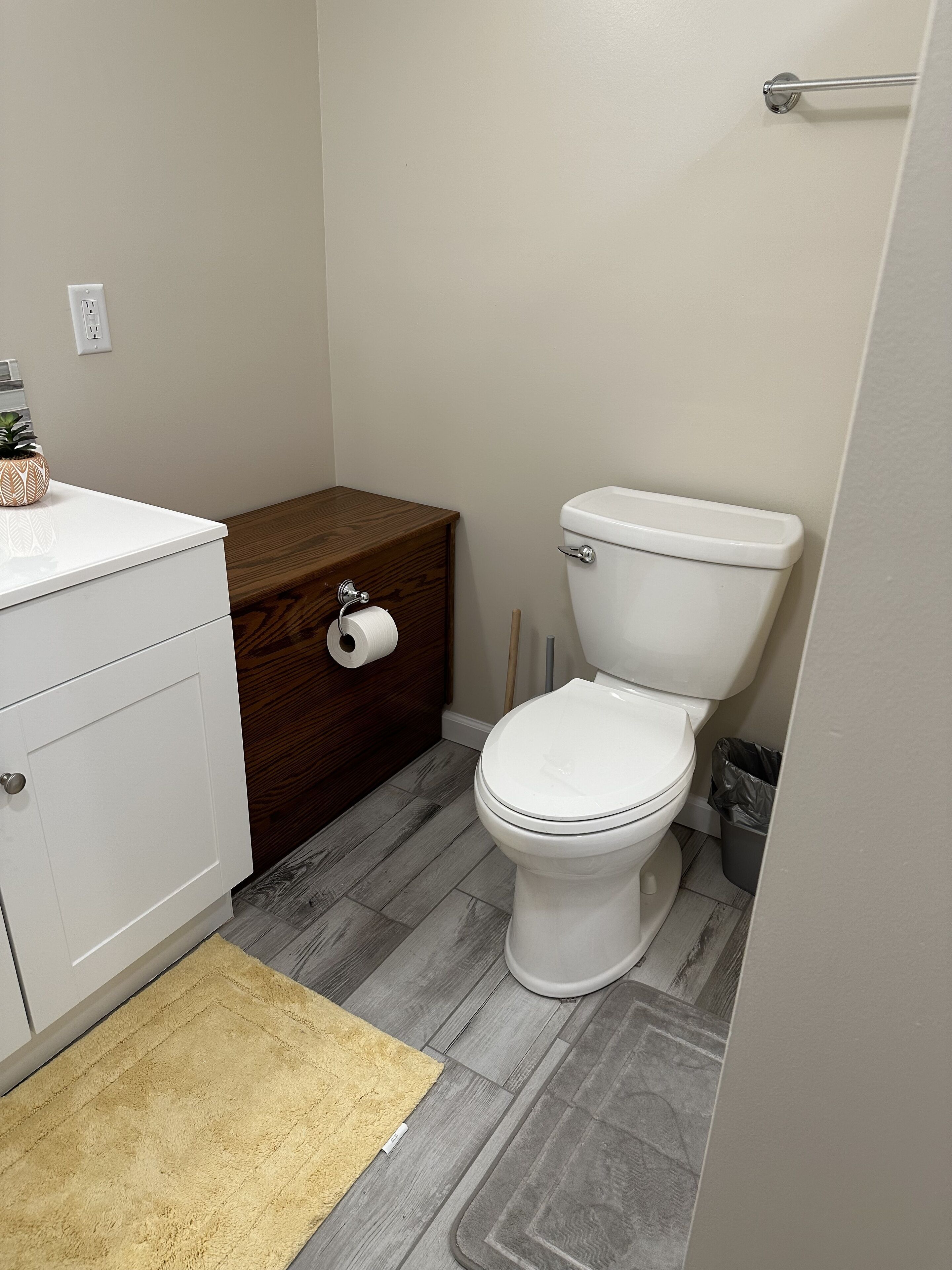 Un bagno con il water, un armadietto in legno, un lavandino bianco e un tappeto giallo.