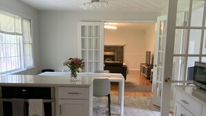 A modern kitchen with white cabinetry, a central island, and a dining area with a gray chair. - Recently Updated, One Level, Attached Garage, Peaceful, Zen-Minimalist Space.  (Avon)