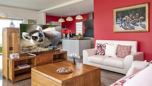 Ein modernes Wohnzimmer mit Flachbildfernseher, Holzunterhaltungseinheit und einem weißen Sofa mit gemusterten Kissen.