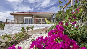 Ein modernes Haus mit rotem Ziegeldach, einem Balkon und einem Garten mit rosa Blumen.