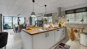 A modern kitchen with a central island, large windows, and a dining area with a view. - 3 bedroom cozy home in Thyholm (Thyholm)