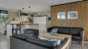 A modern living room with a sofa, a coffee table, and a dining area with a kitchen in the background. - 3 bedroom cozy home in Thyholm (Thyholm)