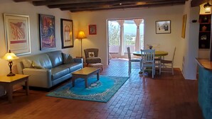 Una sala de estar con sofá, mesa de centro y sillas, un comedor con mesa y sillas, y una cocina con mostrador y estantes.